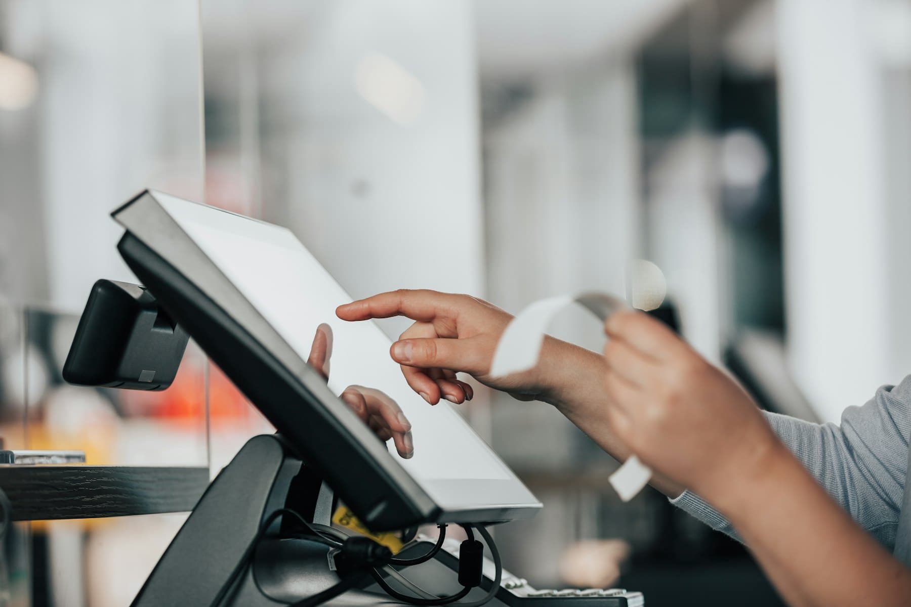 Cashier tapping a point-of-sale screen while handing over a receipt at checkout