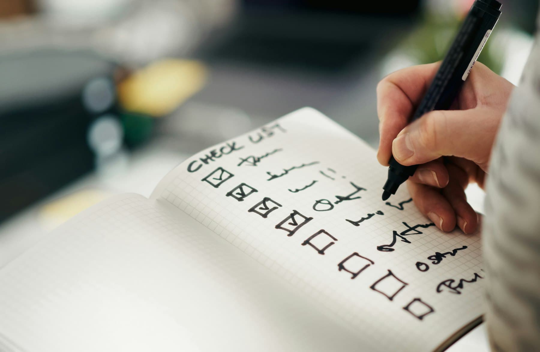 Hand ticking boxes on a handwritten checklist in a notebook