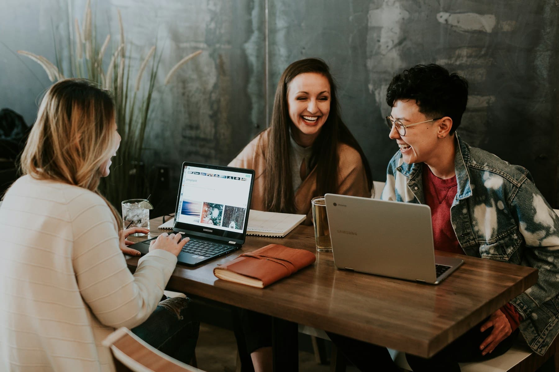 Three coworkers laughing around a table with laptops during a team check-in