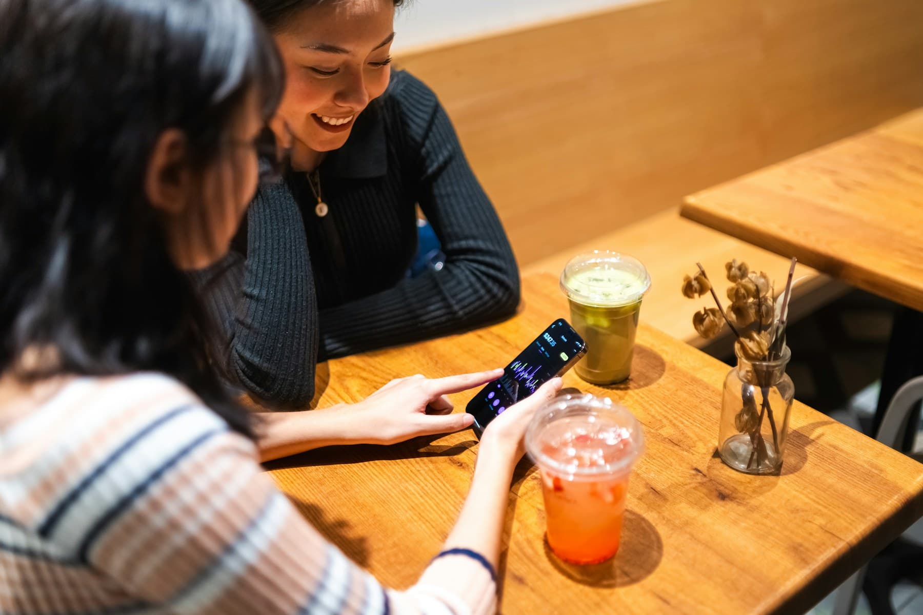 Two friends looking at a smartphone together at a café table